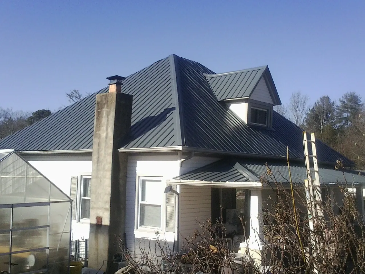 Dark blue standing seam metal roof on a white farmhouse with dormer — Slate & Tile Roof Repair by Roofing Brothers in San Felipe
