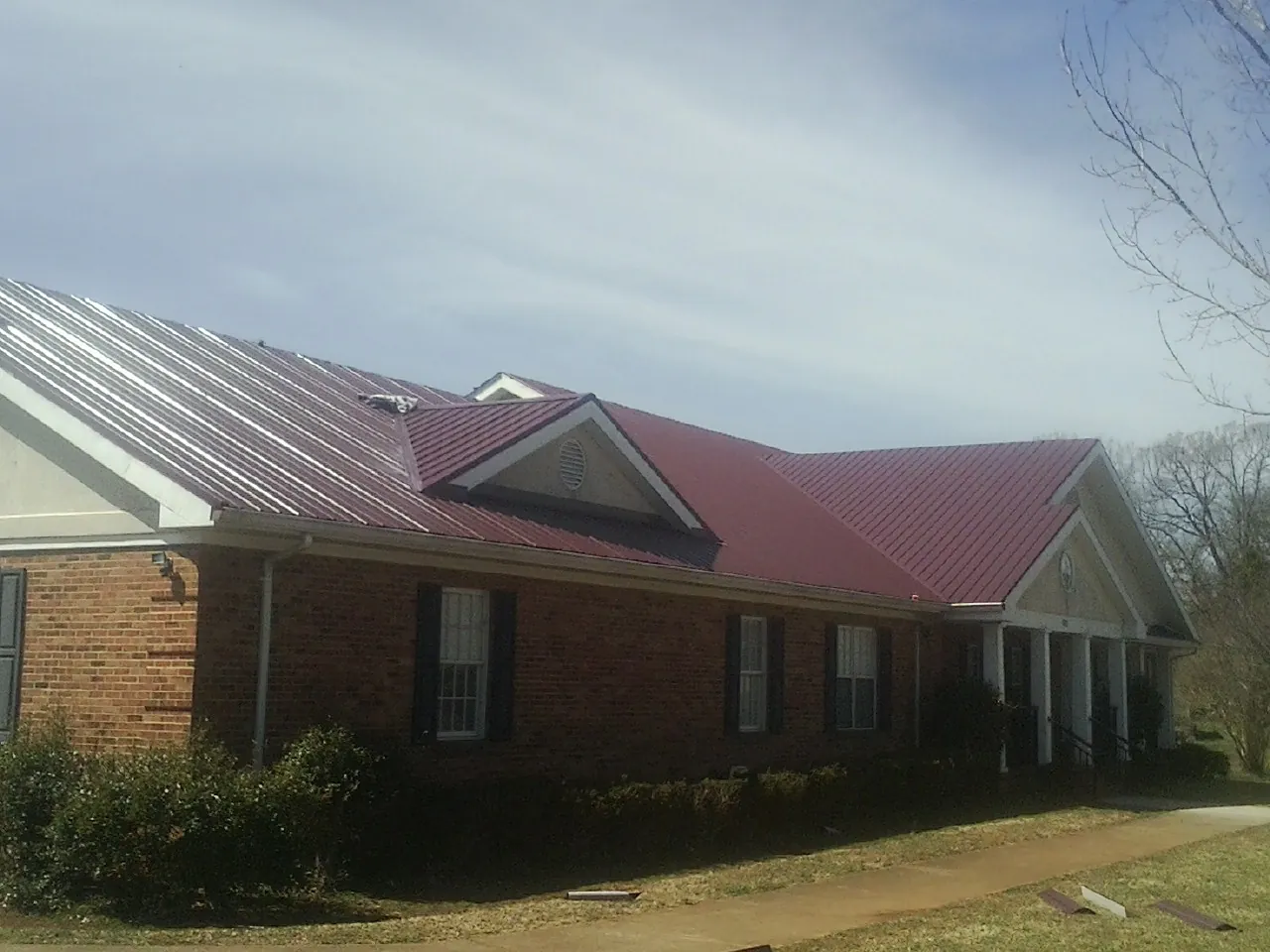 Red metal roof with gabled entries on a long brick building, from a Hail Damage Roof Repair job in San Felipe