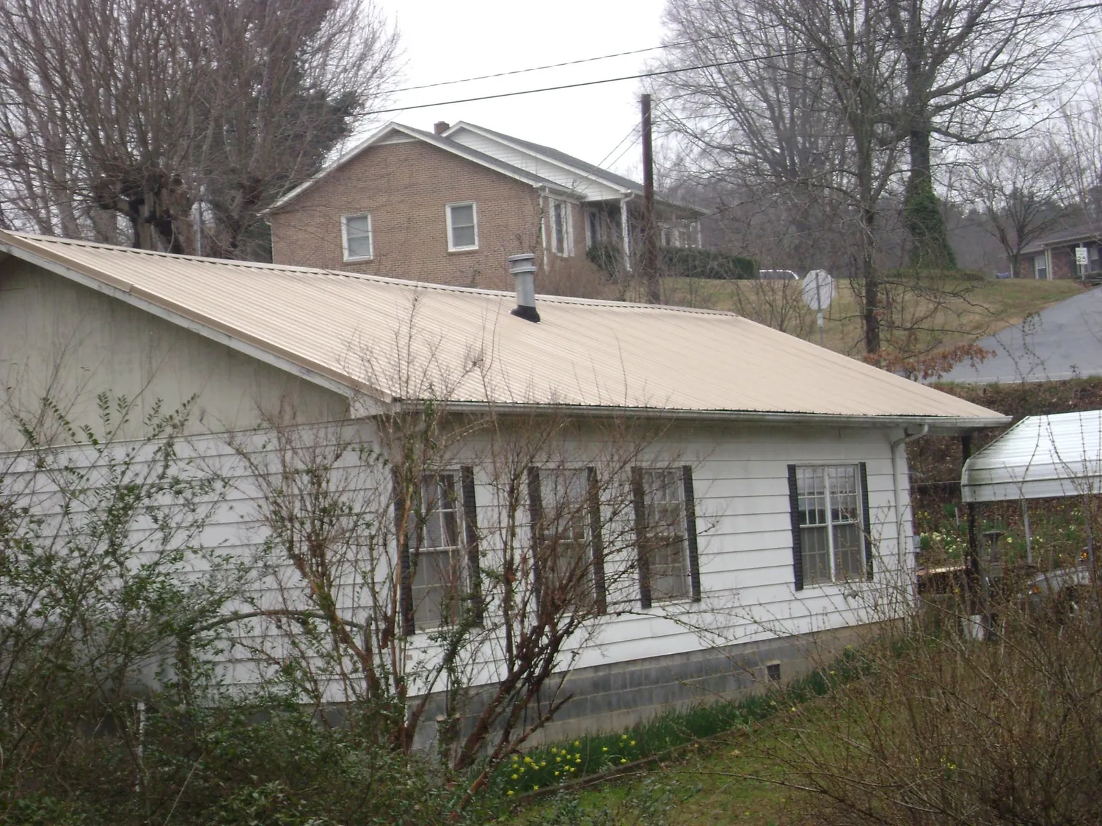 Tan metal roof on a white sided house set into a hillside — Commercial Roofing by Roofing Brothers in San Felipe